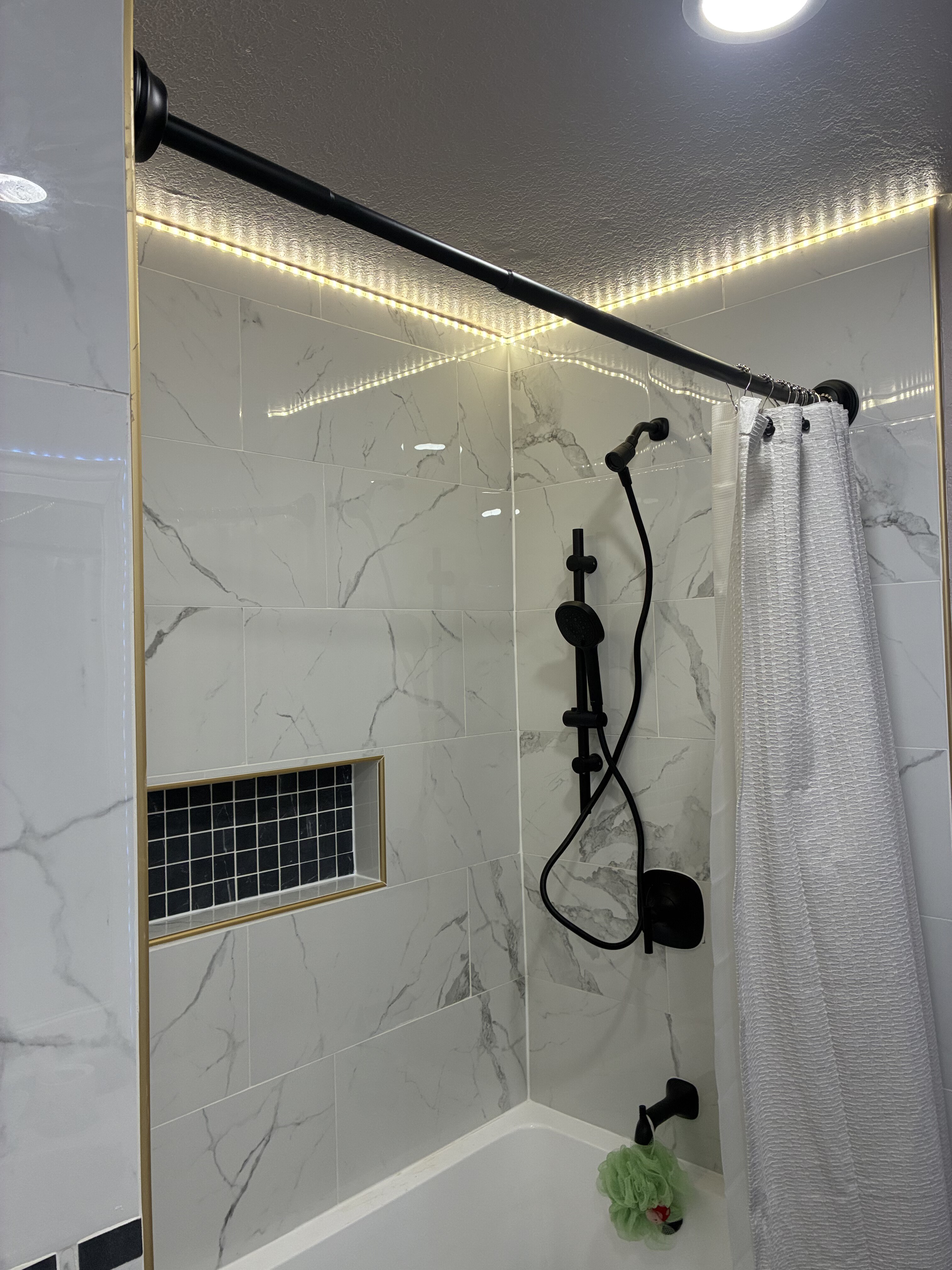 Marble tile tub-shower with gold trim, black mosaic niche and warm LED accent lighting