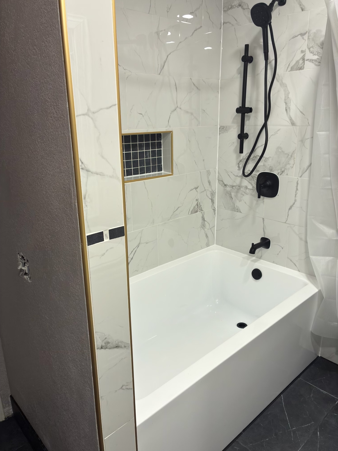Finished marble-tile tub and shower with matte black fixtures and gold trim