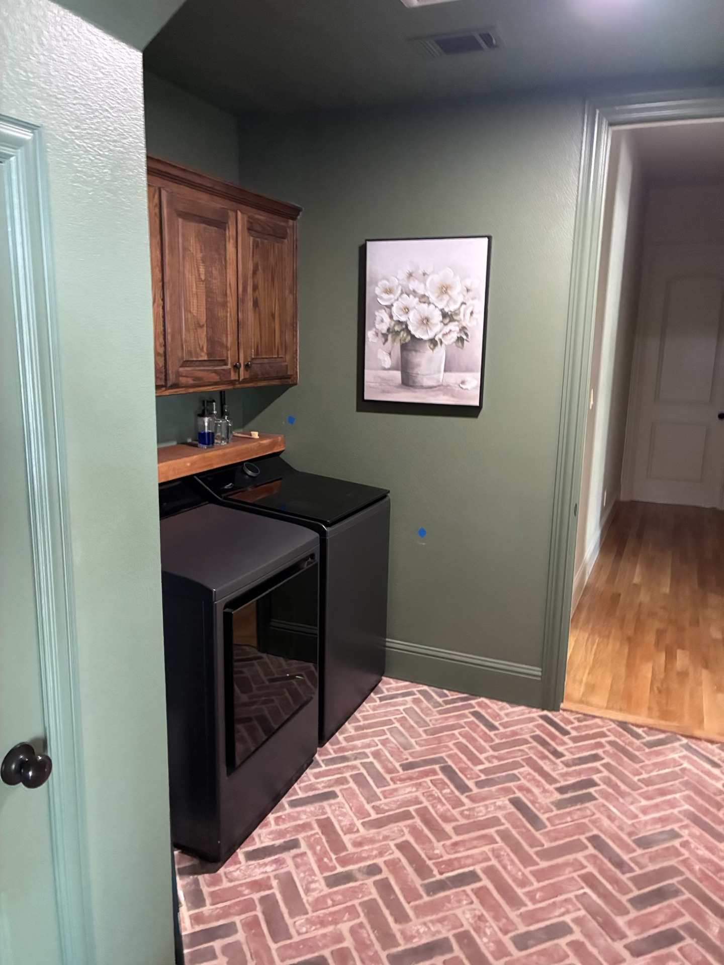 Renovated laundry room with brick herringbone floor and sage green walls